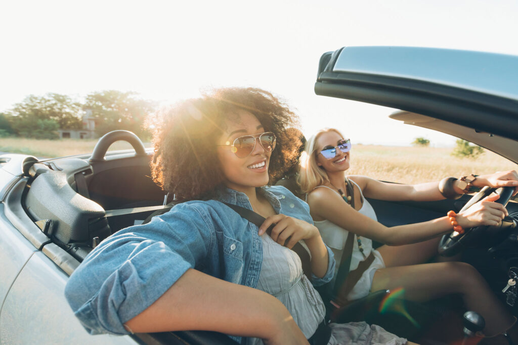 Duas mulheres sentadas em um conversível aproveitam o dia ensolarado.