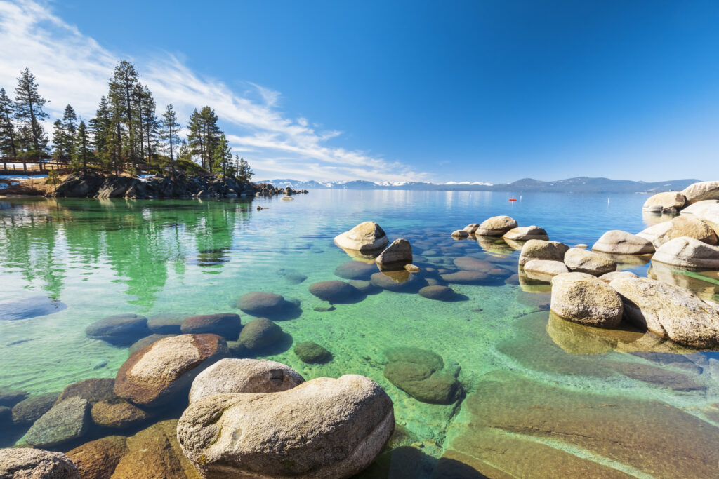 Lake Tahoe rocky shoreline in sunny day, beach with blue sky over clear transparent water