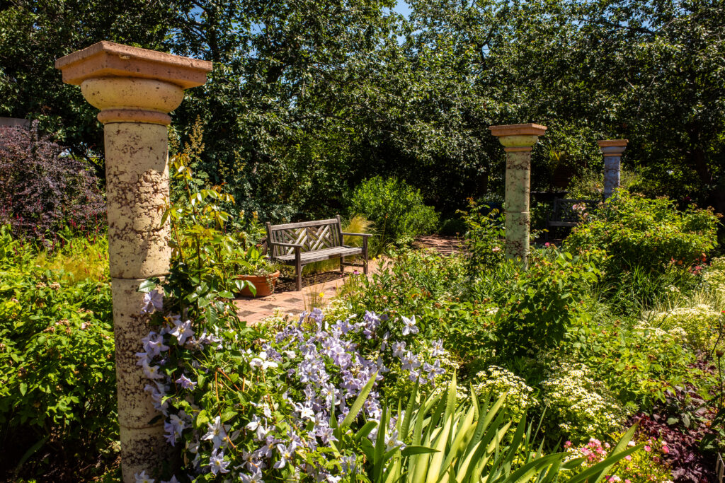 Banco junto a columnas en un exuberante entorno verde lleno de flores en los Jardines Botánicos de Denver.